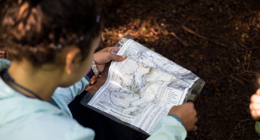 A person sits on the ground and examines a map